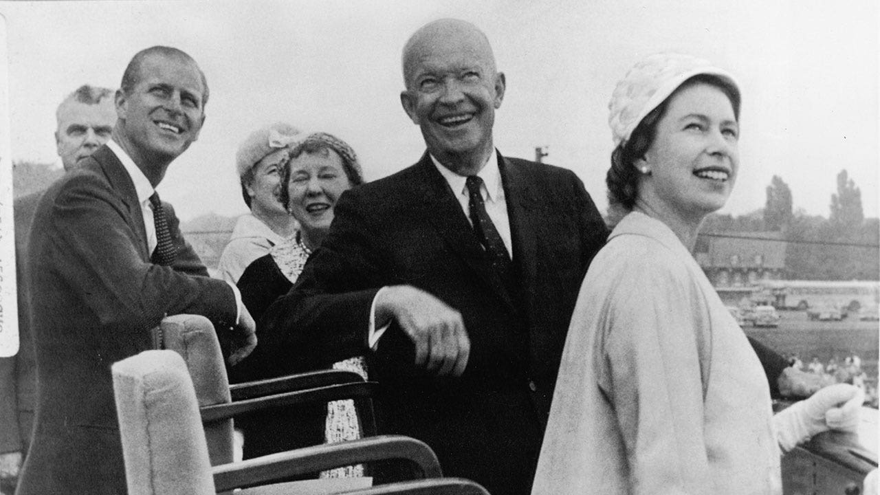 Black and white photo of Queen Elizabeth wearing a coat and a hat and President Eisenhower sitting to her left